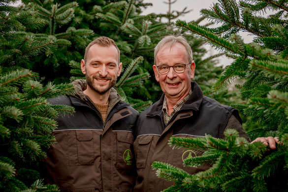 Die Inhaber Sören und Rainer Prüser stehen vor Weihnachtsbäumen.