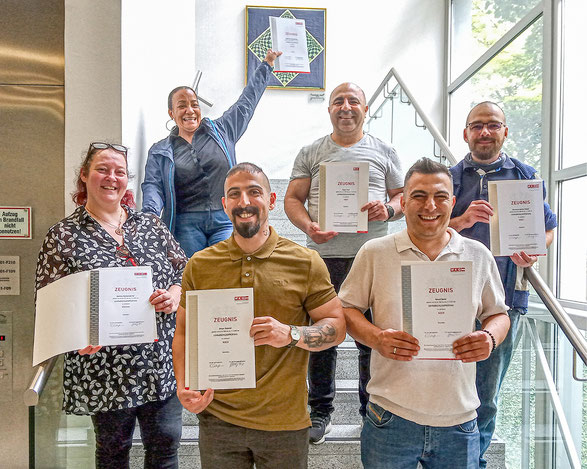 Erfolgreiche Teilnehmer bei Gruppenfoto mit Urkunden auf einer Stiege