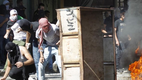 Palestinian protesters take cover from behind barricade as they clash with Israeli troops along the dividing line in Hebron / Photo: archive