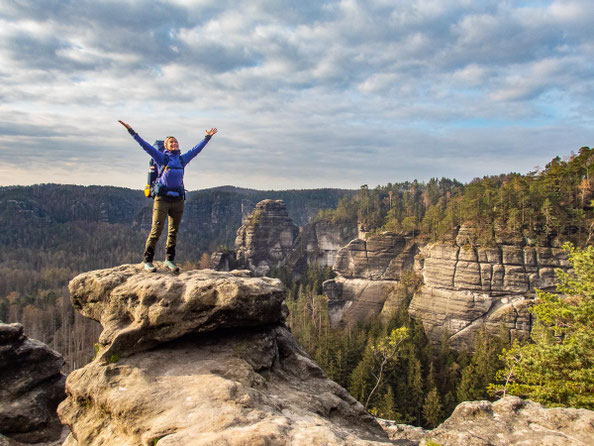 Wanderin auf markanter Sandsteinfelsformation im Elbsandsteingebirge mit Blick über die Sächsische Schweiz