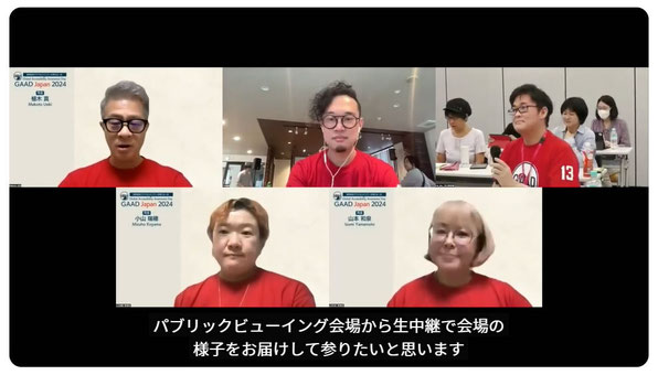 昨年のライブ配信中の画面　3名のスタッフと2名の会場担当者が映っている　2名の会場担当者の背後には各会場の様子が少し見えている　画面の下に字幕があり「パブリックビューイング会場から生中継で会場の様子をお届けしてまいりたいと思います」とある