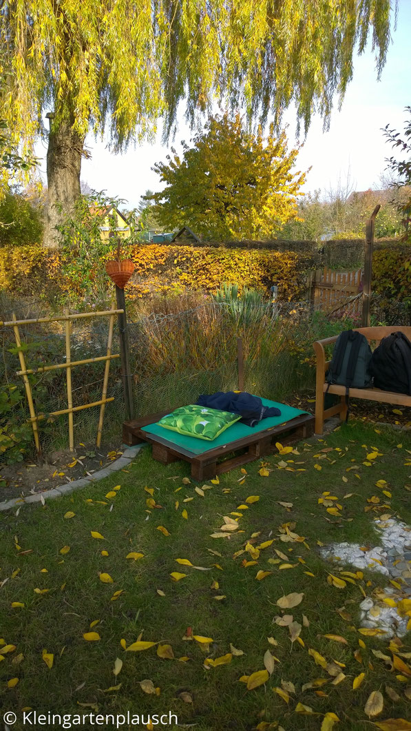 Braun lackierte Palette im Garten, obendrauf grüne Isomatte und grünes Kissen