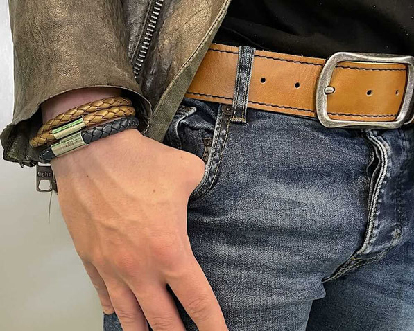 Am rechen Handgelenk eines Mannes befindet sich ein einfach gewickeltes schwarzes Lederarmband mit Edelstahl Magnetverschluss und darüber ein goldfarbenes doppeltes Lederarmband mit Edelstahl Magnetverschluss 