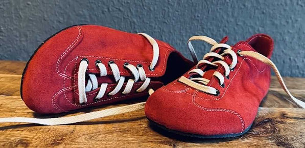 Rote Wildleder Barfußschuhe mit weißen Senkeln liegen auf einem Tisch