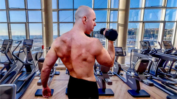 A muscular man performing dumbbell curls in a high-end gym with panoramic sea views in Monaco, showcasing elite strength training and personal coaching services