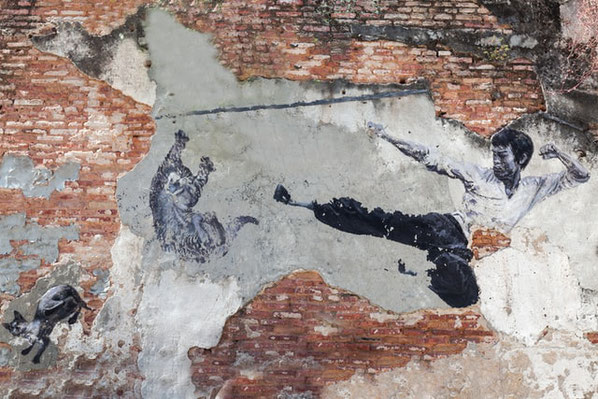 Ein Bild von Bruce Lee auf einer Mauer. Er vollführt einen Sprungtritt.