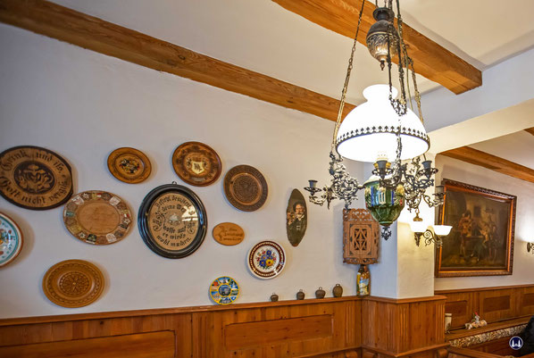 Blick in einen der Gasträume im Erdgeschoß. Alte Lampen, Bilder und Porzellanteller sowie die Holzverkleidung der Wände und die alten Deckenbalken vermitteln einen rustikalen süddeutschen Eindruck.