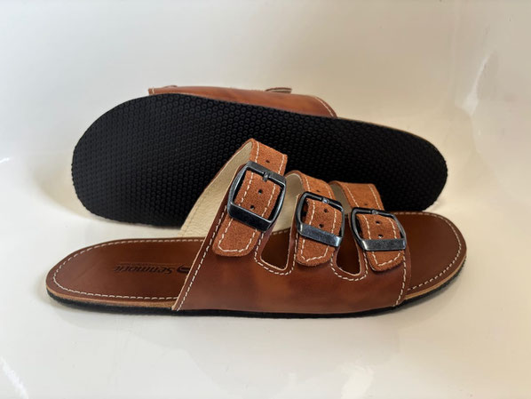 Pantolette aus braunem pflanzlich gegerbten Leder mit drei Riemen und drei Metallschnallen.