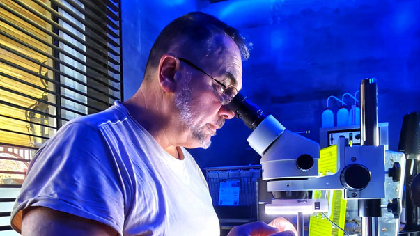 Frédéric est en train de regarder au travers d'une loupe binoculaire sur un fond de laboratoire ambiance bleue.