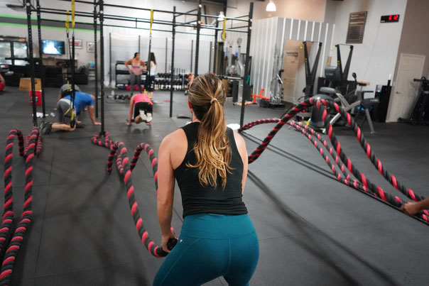In einem Fitnessstudio trainieren Sportler im Funtional Bereich. Die Frau im Vordergrund trainiert mit den Battle Ropes die Kraftausdauer.