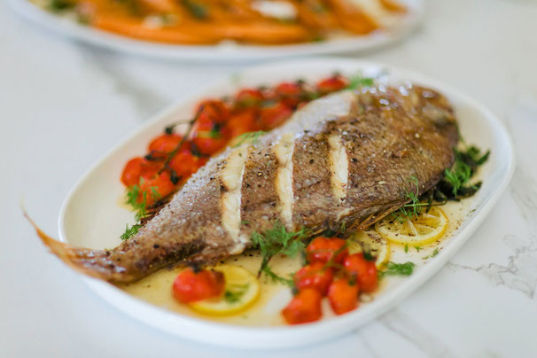 Photographie d'un plat culinaire très joli où on voit un poisson cuit nappé de Miel de Manuka de Nouvelle-Zélande avec ses petits légumes (citron, thym, tomates) dans un restaurant gastronomique