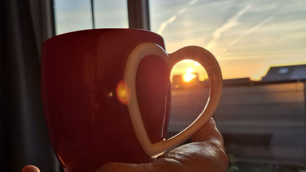 Kaffeebecher im Vordergrund - im Hintergrund Blick aus Fenster zur Sonne