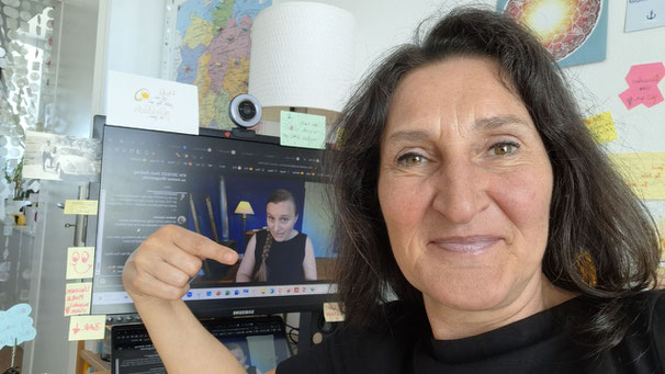 Frau steht am Schreibtisch mit Laptop - darauf ist eine andere Frau zu sehen