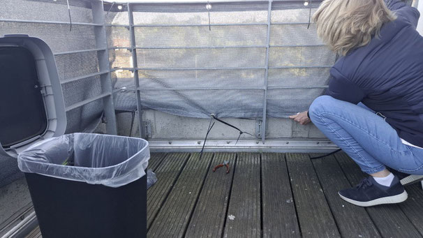 Frau befestigt Sichtschutz auf Balkon