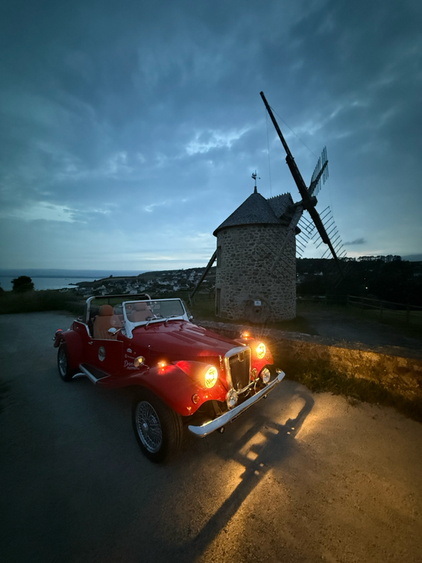 Spartan garée devant un moulin à vent en bord de mer à la tombée de la nuit, en Bretagne.