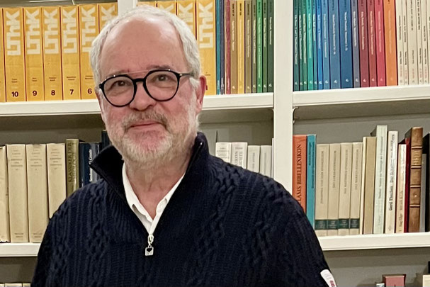 Christoph Winterhalter mit Brille in einer Bibliothek, vor farbigen Buchreihen, ruhige und konzentrierte Atmosphäre.