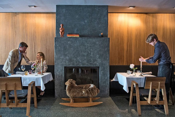 Elegante ristorante Vinzenz - zum feinen Wein a Vipiteno con camino moderno, tavoli apparecchiati, atmosfera romantica, servizio al tavolo e accogliente pecora a dondolo in legno come decorazione.