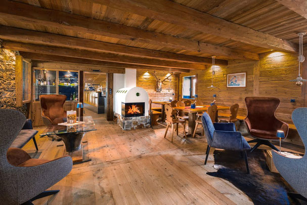Gemütliche Stube der Starkenfeldhütte mit Holzdecke, Kaminfeuer, rustikalen Holztischen und modernen Sesseln – perfekte Mischung aus alpinem Charme und Komfort.