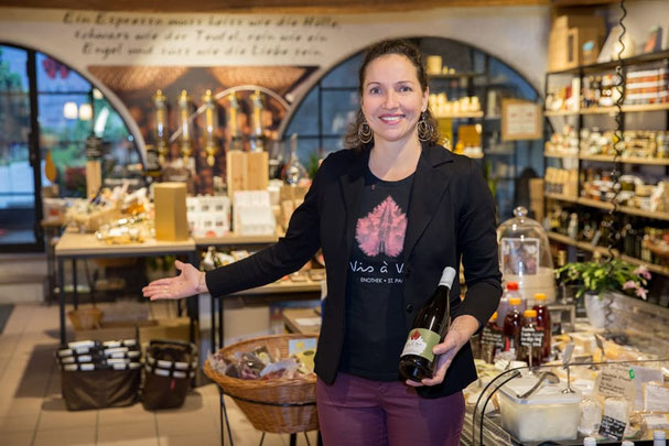 Stefanie, die Inhaberin des Vis à Vis Wein- und Genusshauses in St. Pauls präsentiert eine Weinflasche zwischen Feinkost und Delikatessen in gemütlicher Vinothek