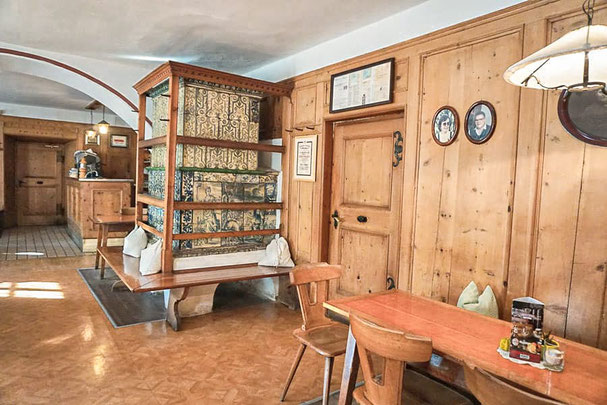 Gemütliche Stube im Gasthaus Alte Post in Atzwang mit traditioneller Holzvertäfelung, Kachelofen, Holztischen und historischer Dekoration – ein Ort voller Charme.