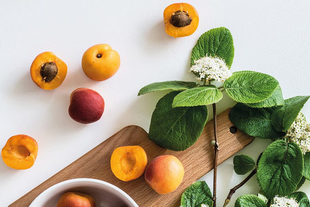 Albicocche fresche della Val Venosta su un tagliere di legno, accompagnate da foglie verdi e fiori, ideali per la Festa del Marmo e delle Albicocche a Lasa.