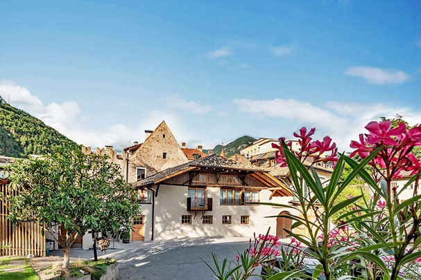 Weingut Schmid Oberrautner in Bozen-Gries mit historischem Gebäude, Innenhof, Holzbalkonen und blühenden Oleandersträuchern vor alpiner Kulisse.