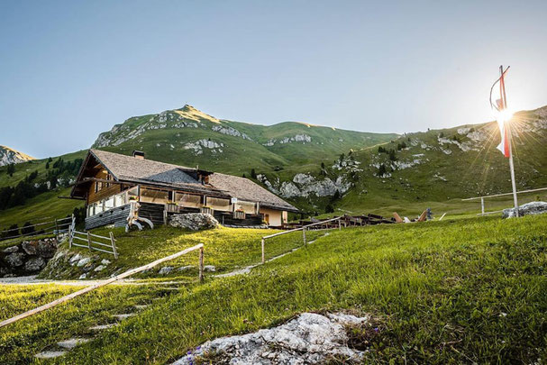 Die Gampenalm in Villnöss bei Sonnenaufgang, umgeben von grünen Almwiesen und Bergen – beliebtes Ausflugsziel mit Hütte und Blick auf die Dolomiten.