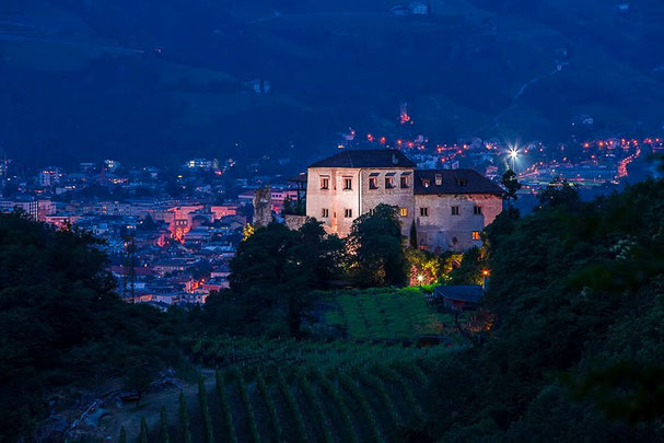 Vista sul castello Castel Flavon illuminato a festa sui tetti di Bolzano di notte: uno scenario suggestivo con vigneti e vista panoramica sulla Valle dell'Adige.