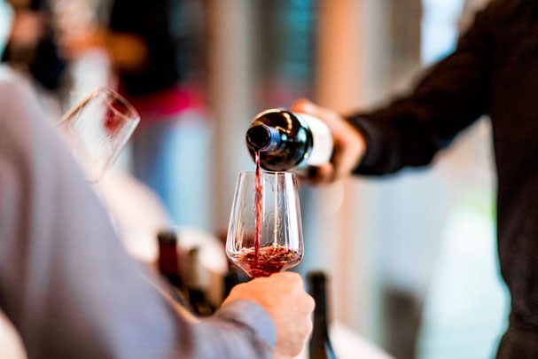 Un esperto di vini versa il vino Schiava in bicchieri, circondato da bottiglie di vini pregiati: una scena dal Trofeo Schiava al vigilius mountain resort.