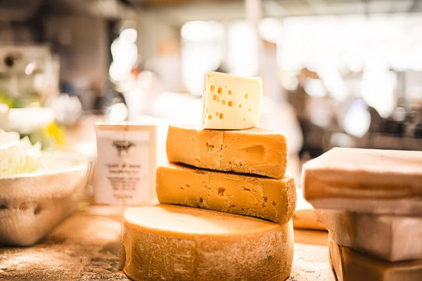 Diverse forme e pezzi di formaggio a pasta dura impilati su un banco del mercato durante il festival del formaggio, sullo sfondo l'atmosfera sfocata del festival.