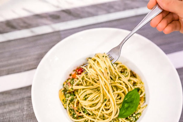  Spaghetti alle erbe aromatiche e pomodorini in un piatto bianco, arrotolati con la forchetta, serviti su un tavolo chiaro con tovagliolo di stoffa – presentati in modo fresco e appetitoso
