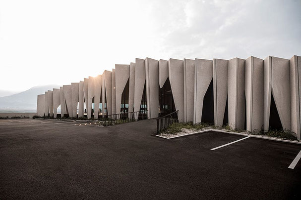 Moderne Fassade der Kellerei Kurtatsch in Südtirol mit skulpturalen Betonlamellen, klaren Linien und Blick auf die umliegenden Weinberge bei sanftem Morgenlicht.