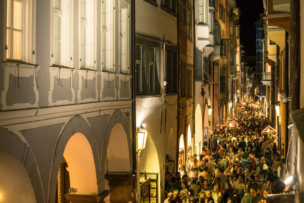 Folla durante la Calici di Stelle a Bolzano sotto i portici storici di notte con stand di vino e illuminazione suggestiva.