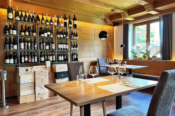 Steakhouse Anny a Marlengo con elegante parete dedicata ai vini, tavoli apparecchiati in stile moderno, caldi interni in legno e luminosi posti a sedere vicino alle finestre con orchidee: un ambiente elegante dove gustare ottimi piatti.