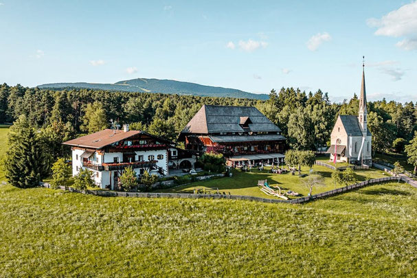 Ansitz Kematen bei Klobenstein am Ritten mit Restaurant, Hotel und kleiner Kirche, umgeben von Wiesen und Wald, sonnige Lage mit Panoramablick auf die Südtiroler Bergwelt.