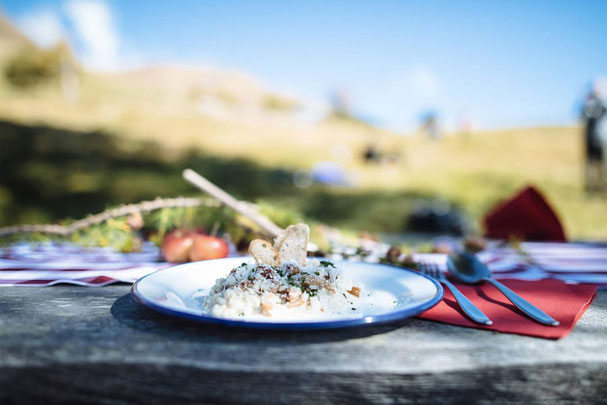 Gourmetgericht im Freien auf Holzbank serviert, aufgenommen bei Sonnenschein in der Südtiroler Berglandschaft beim Tallner Sunntig im Hirzergebiet.