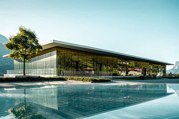 Cantina di Merano: enoteca panoramica a Marlengo caratterizzata da una moderna architettura in vetro, riflessi sull'acqua e vista sui vigneti del Meraner Land
