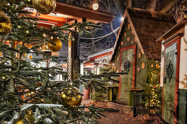 Festlich geschmückter Weihnachtswald bei Forst in Algund mit beleuchtetem Tannenbaum, goldenen Kugeln und liebevoll gestalteten Hütten – stimmungsvolle Adventsatmosphäre in Südtirol.