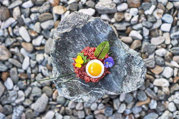Tartara di manzo con uovo di quaglia, fiori commestibili ed erbe aromatiche, servita con arte su pietra naturale al ristorante Eggile di Valles, in Alto Adige.