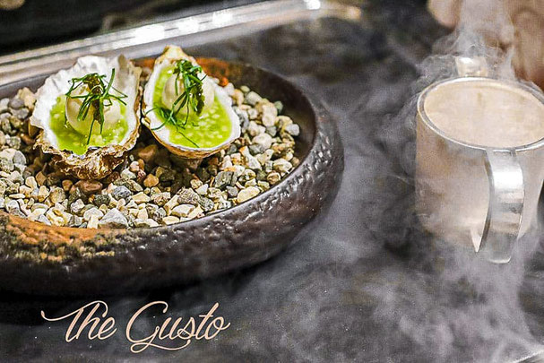 Piatto gourmet al Gusto Festival del Romantik Hotel Stafler: ostriche servite su ciottoli con erbe aromatiche, accompagnate da una bevanda fumante.