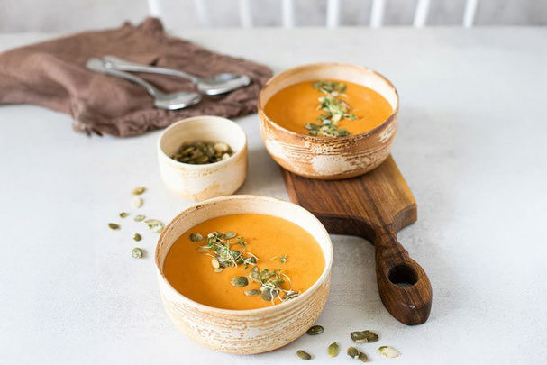 Cremige Kürbissuppe mit Kürbiskernen, serviert in einer Keramikschüssel auf rustikalem Holztisch, dazu ein Glas Rotwein und ein Löffel auf Stoffserviette bei der Gruppe Südtiroler Gasthaus