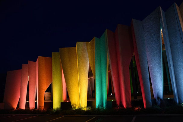 Facciata illuminata della Cantina Kurtatsch di notte: lamelle in calcestruzzo dai colori dell'arcobaleno risplendono suggestivamente durante l'evento “Aperitivo Panoramico” in Alto Adige.
