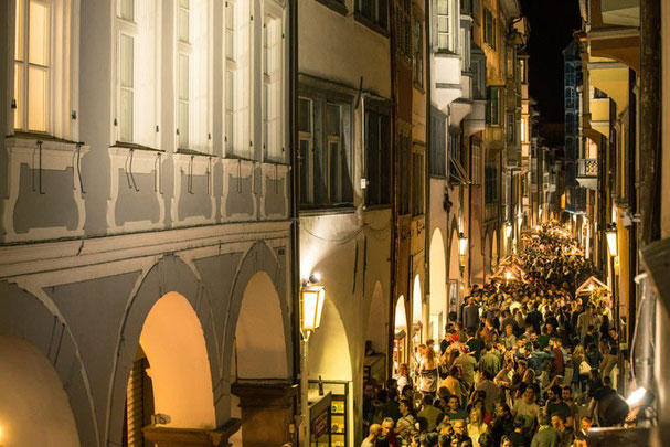 Menschen bei der Lorenzinacht in Bozen unter den historischen Lauben bei Nacht mit Weinständen und stimmungsvoller Beleuchtung.