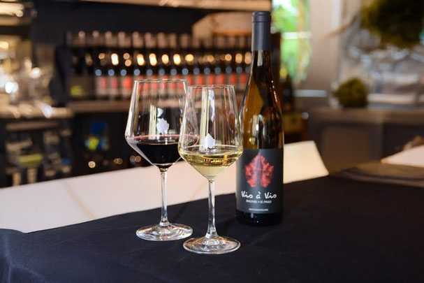 Weinverkostung im Vis à Vis Enothek St. Pauls/Eppan: Rot- und Weißwein im Glas mit Vis à Vis Flasche, stilvolles Ambiente für Genuss und Degustation.