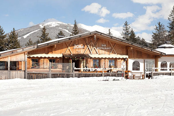 „Restaurant Jora Mountain Dining in San Candido, umgeben von verschneiten Bergen, bietet eine rustikale Atmosphäre und ist bekannt für exklusive Events wie 'Pasta on the Rocks'.”