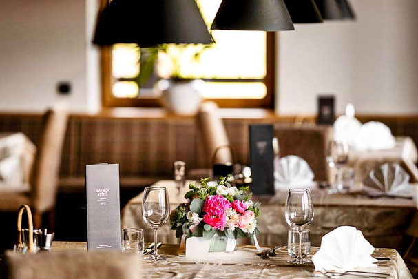 Tavoli elegantemente apparecchiati nel ristorante Rommisa a Vila di Sopra con tovaglioli in stoffa, calici e luce calda in un’atmosfera accogliente.