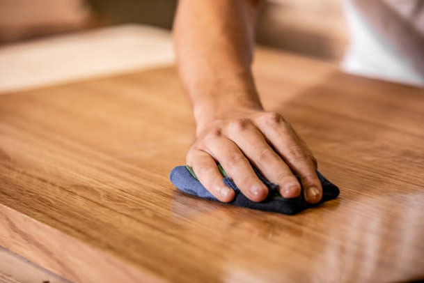 Hand trägt Holzöl auf eine Tischplatte auf