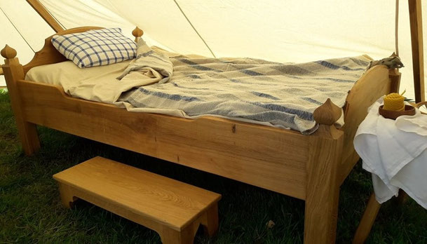 Gotisches Bett in einem Zelt : vor dem Bett steht eine Fußbank, am Fußende ein Schemel, mit einem Handtuch und einer Wachskerze. Im Bett Bettzeug nach historischen Vorlagen, ein Kissen im kariertem Leinenbezug, Laken und eine gestreifte Wolldecke 
