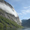 Wasser, Bäume, Felswände und Wolken ziehen sich durch den Geirangerfjord