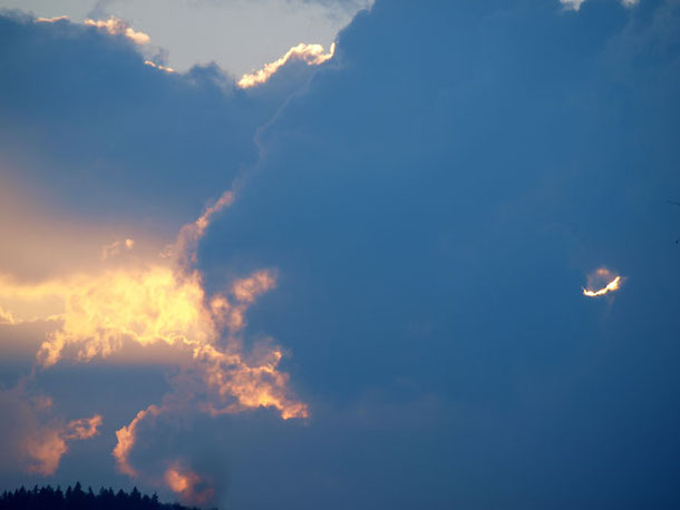 Gewitterwolken mit einer Sonnenscheinöffnung über einem Wald auf der Schwäbischen Alb